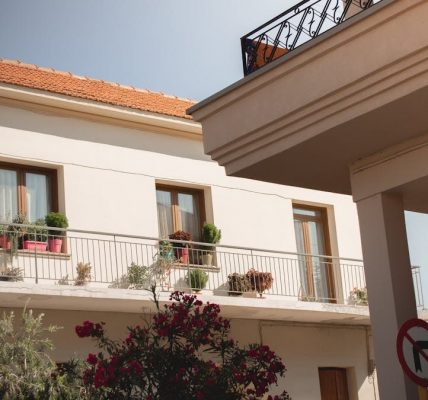 Traditional Greek house facade with potted plants and balcony details.